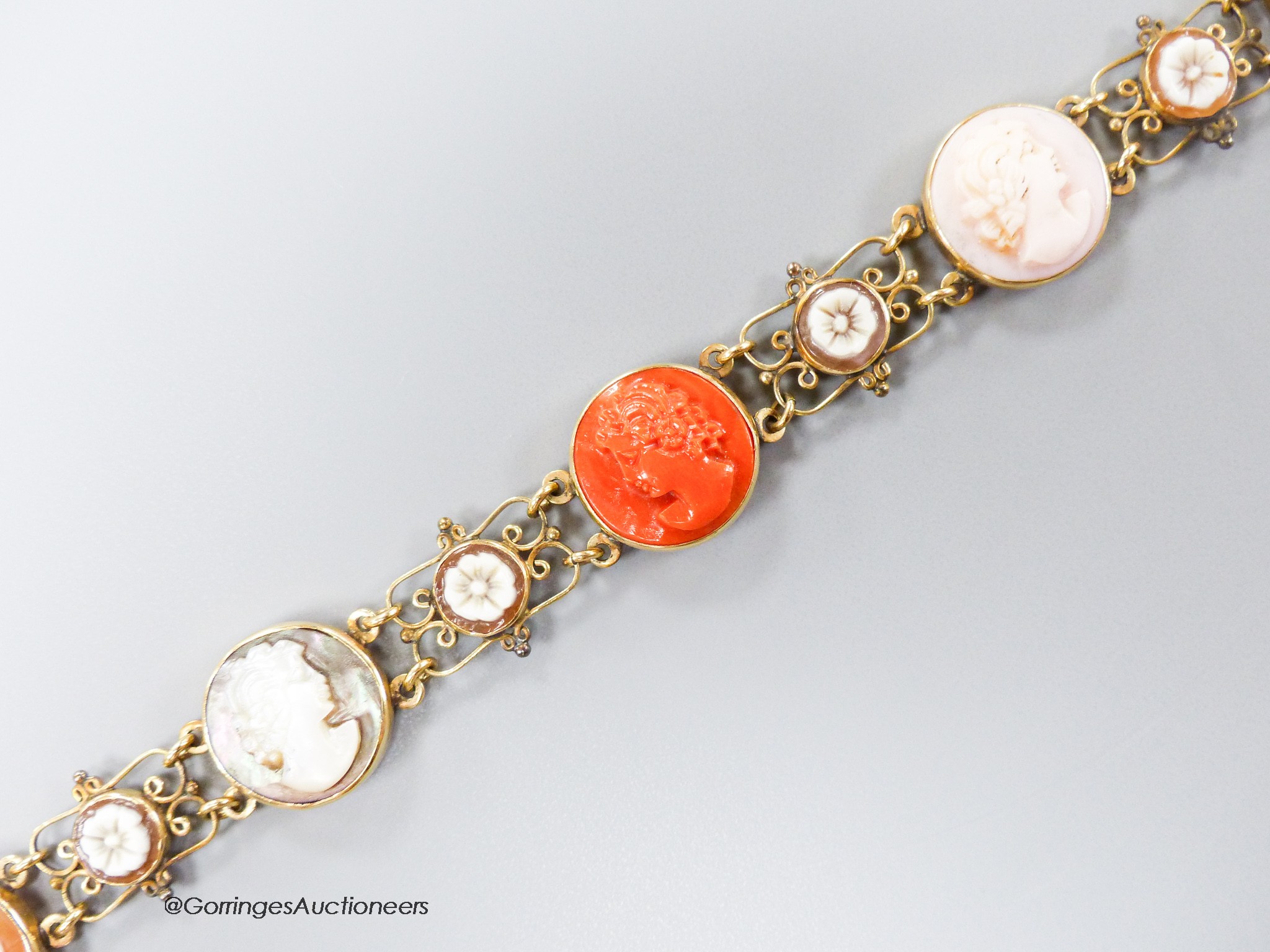 A 14k yellow metal, multi carved cameo and flowerhead set bracelet, including paua shell, shell and coral, carved with the busts of ladies, to dexter and sinister, 16.5cm, gross weight 13.5 grams.